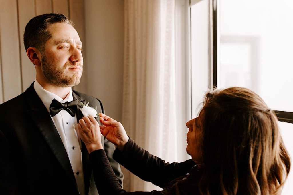 A grooms mother puts on his white flower boutonniere on his wedding day.