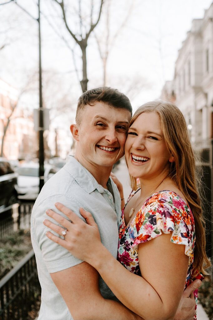 A couple embrace and smile at the camera while standing on a Chicago sidewalk in the spring.