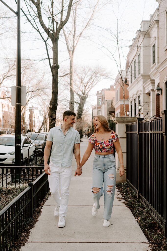 A couple walk hand in hand and laugh on a sidewalk in Chicago
