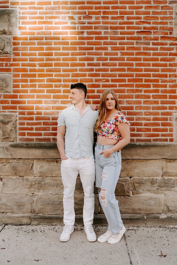 A couple stand side by side in front of a brick wall in Chicago while looking in opposite directions.