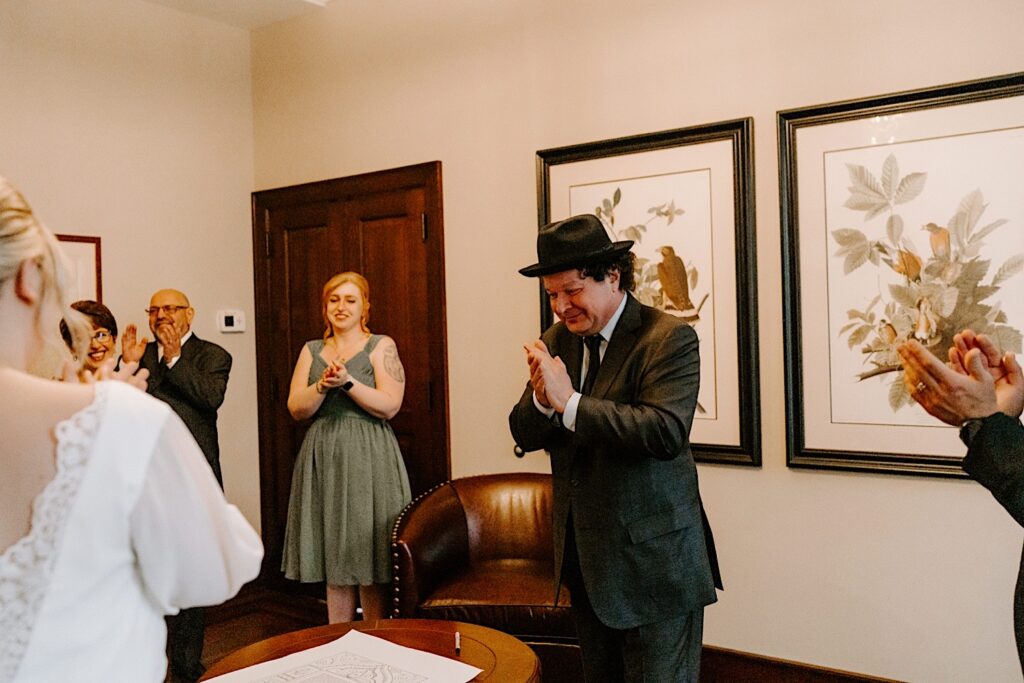 A Rabbi and guests clap after a bride and groom sign their wedding documents.