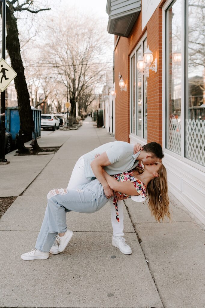 A man dips a woman towards the ground and kisses her in front of a brick building in Chicago