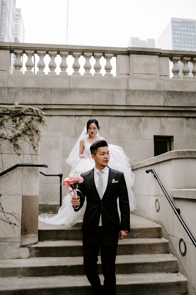 A couple in their wedding attire walk down a staircase next to a bridge in Chicago.