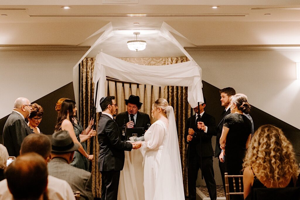 A bride and groom look at one another while the Rabbi gives a speech at their wedding ceremony in Barrington's White House