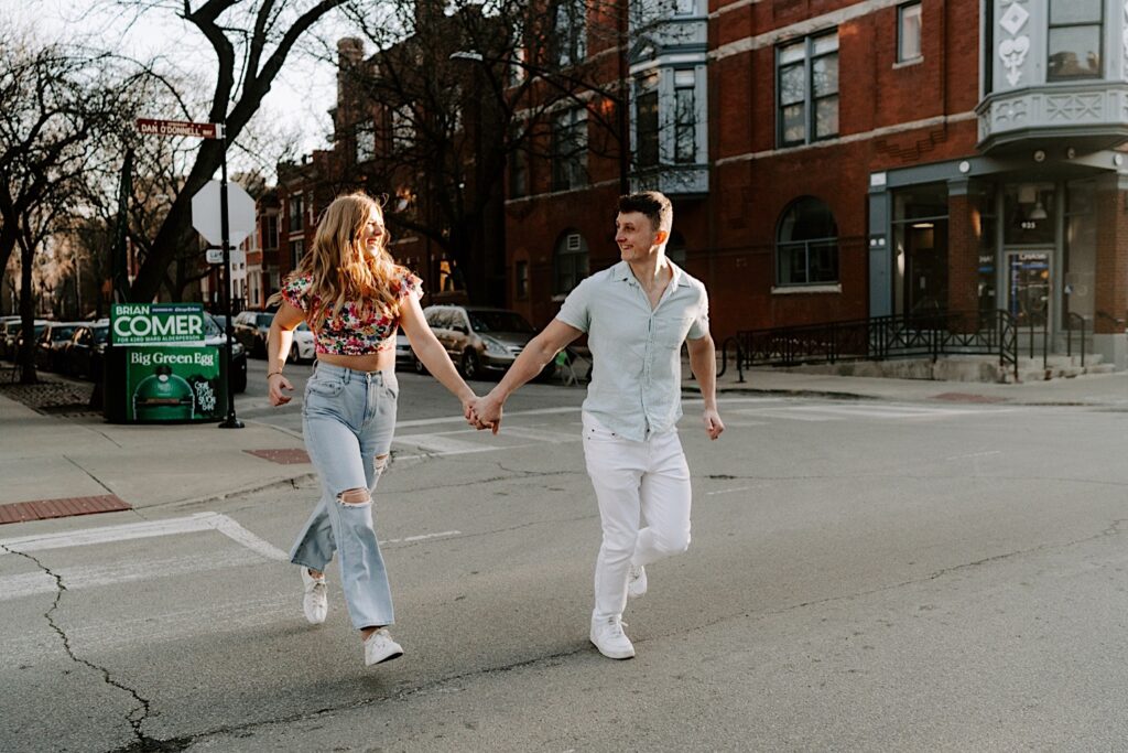 A couple walk across the street together while holding hands and laughing during their session in Lincoln Park