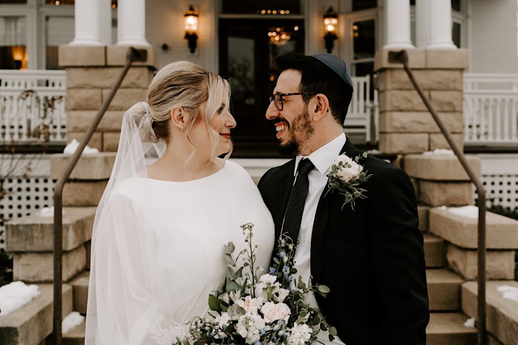 A bride and groom outside their wedding venue, Barrington's White House,  smile at one another