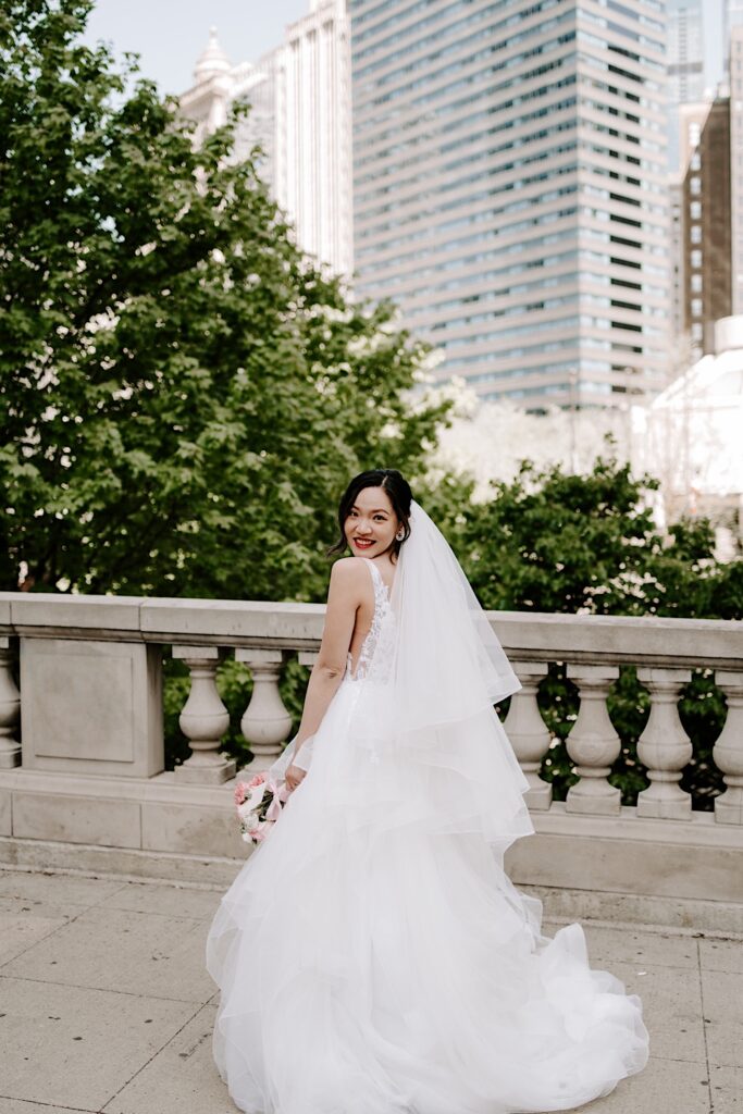 A bride in her wedding dress smiles over her shoulder at the camera in Chicago