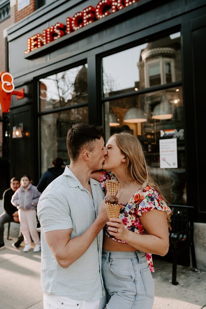 A couple kiss outside of a Jeni's Ice Cream shop in Chicago while holding ice cream cones.