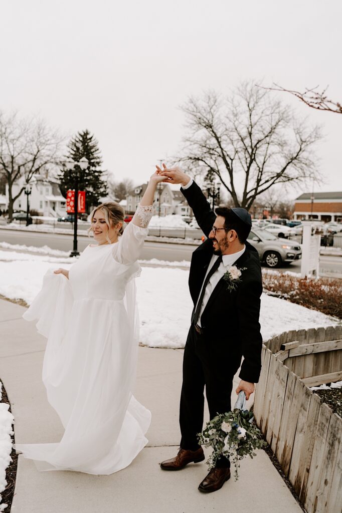 A groom twirls his bride outside with snow on the ground behind them
