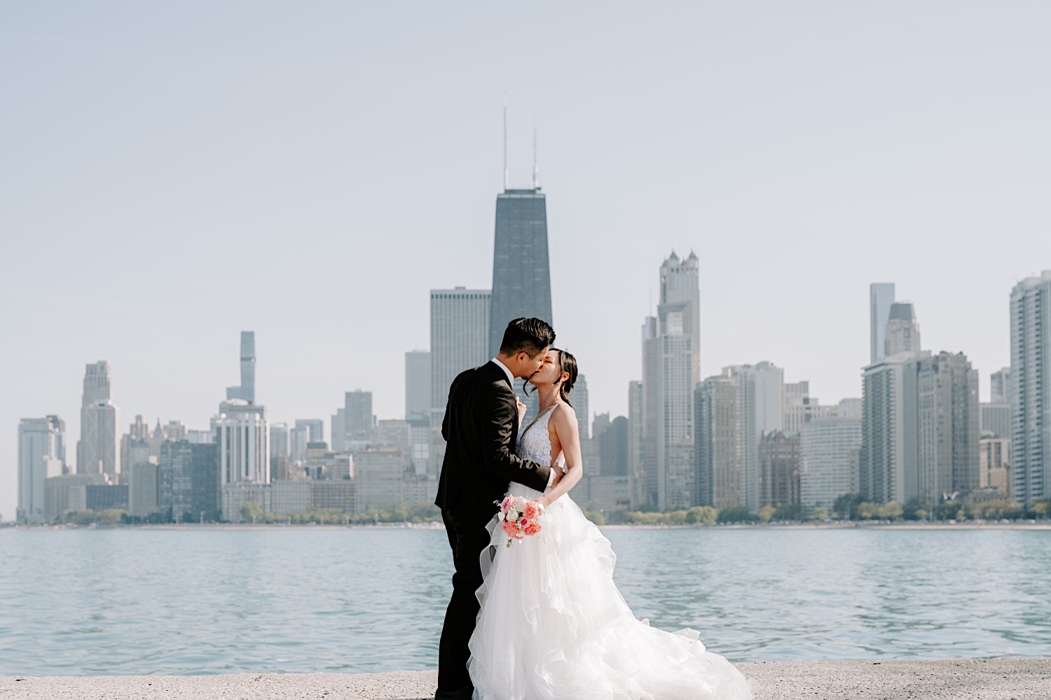 A bride and groom kiss while in their wedding attire at North Avenue Beach in Chicago during their newlywed session