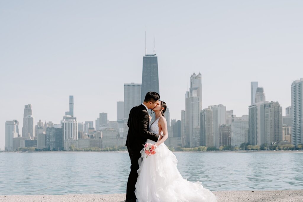 A bride and groom kiss one another while in their wedding attire at North Avenue Beach in Chicago during their newlywed session.