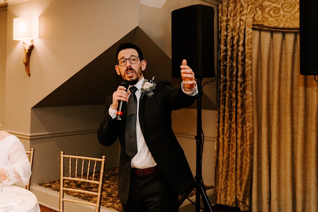 A groom holding a microphone gives a speech during his wedding reception.