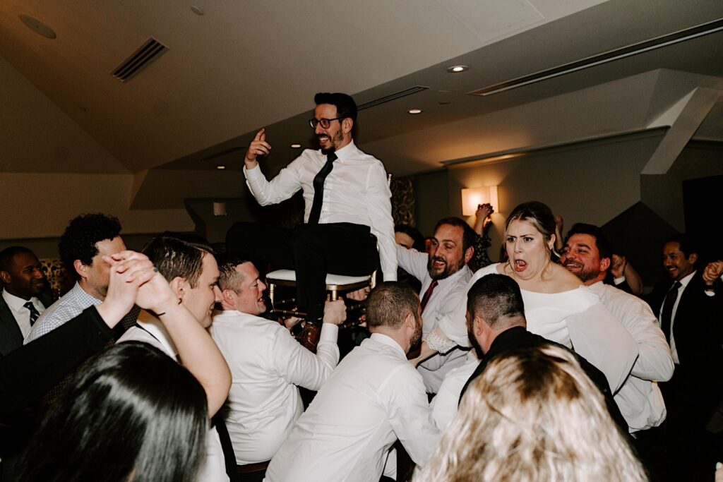 A bride and groom are lifted in the air while sitting in chairs during their wedding reception at Barrington's White House.
