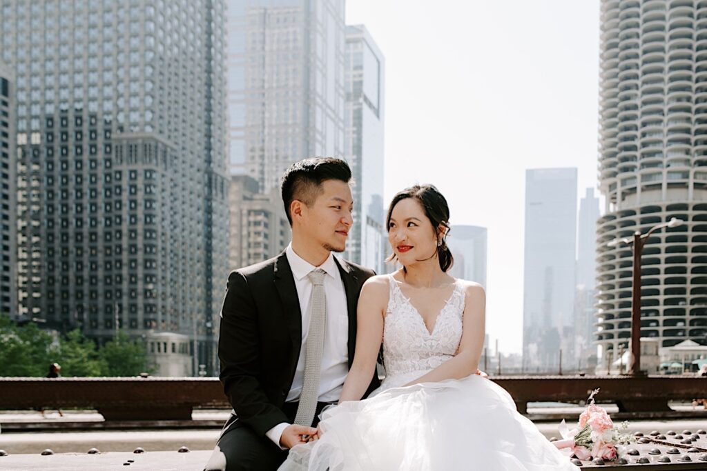 A couple in Chicago sit on a bridge next to each other in their wedding attire during a newlywed session.