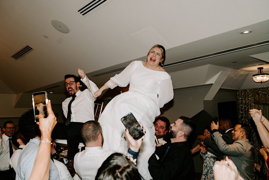 A bride and groom are lifted in the air while sitting in chairs during their wedding reception at Barrington's White House.