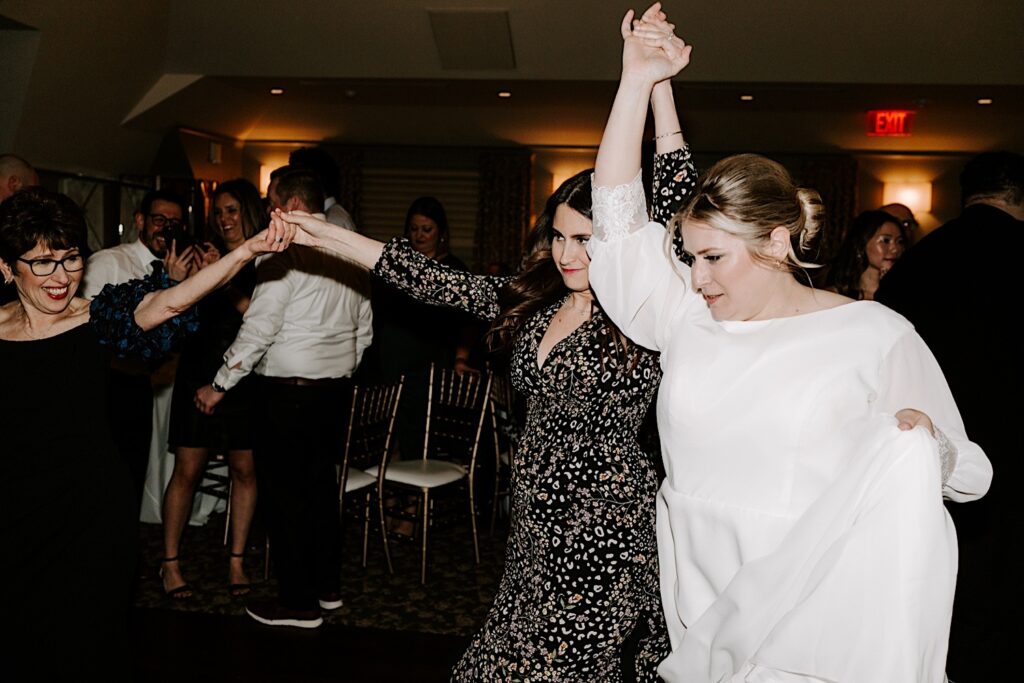 A bride dances with a friend while at her wedding reception.