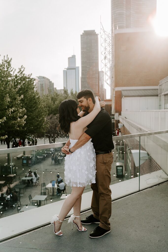 A couple embrace and are about to kiss while standing on a balcony at Navy Pier looking out over the Chicago skyline