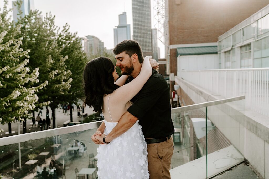 A couple embrace and are about to kiss while standing on a balcony at Navy Pier looking out over the Chicago skyline during their engagement session
