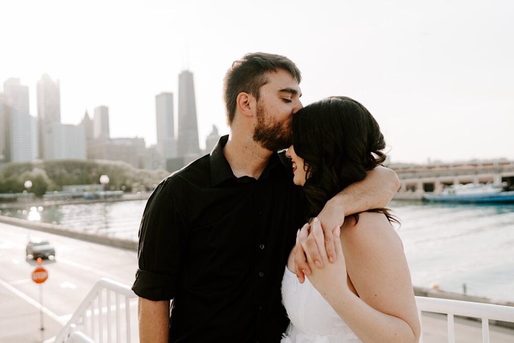 During their engagement session a man kisses a woman on her forehead at Chicago's Navy Pier with the water and skyline in the background
