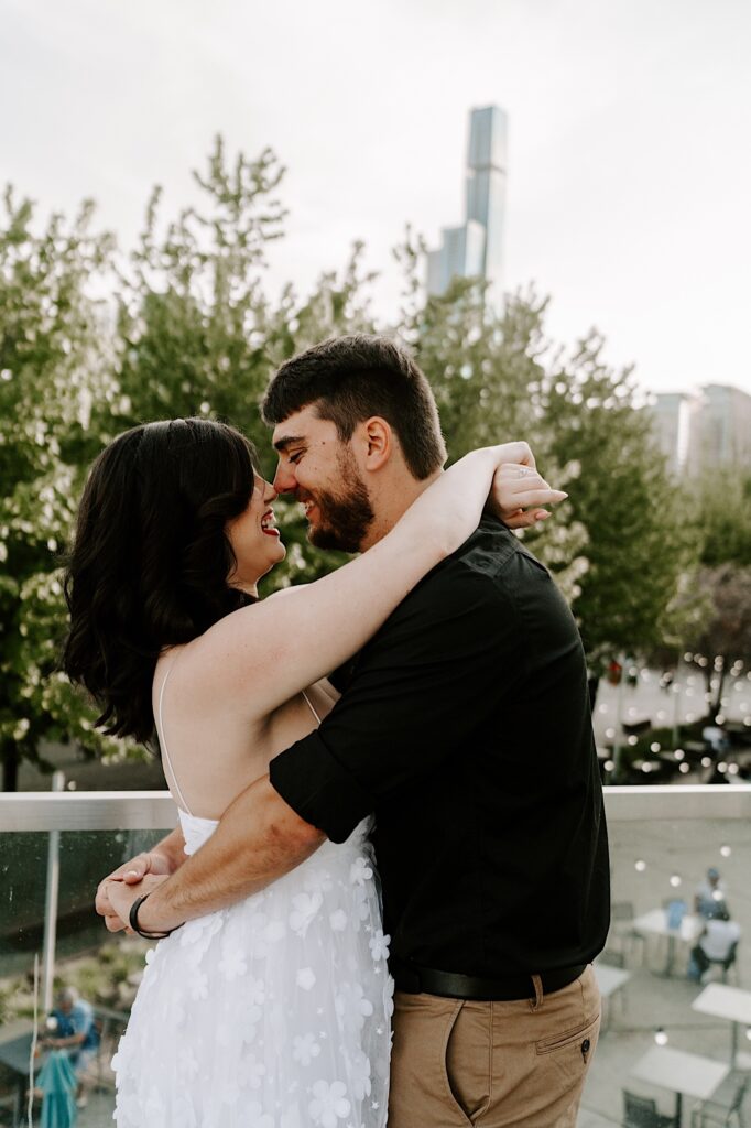 A man and woman embrace and smile at one another at Chicago's Navy Pier with the city skyline behind them