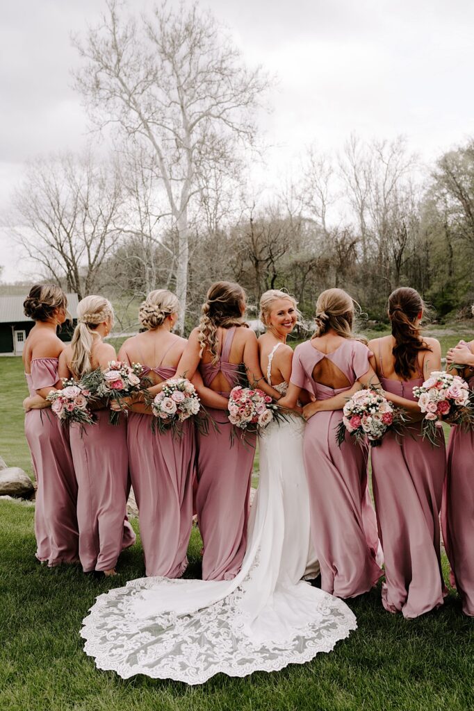 A bride smiles over her shoulder at the camera while her bridesmaids on either side of her look ahead while they all stand in a field