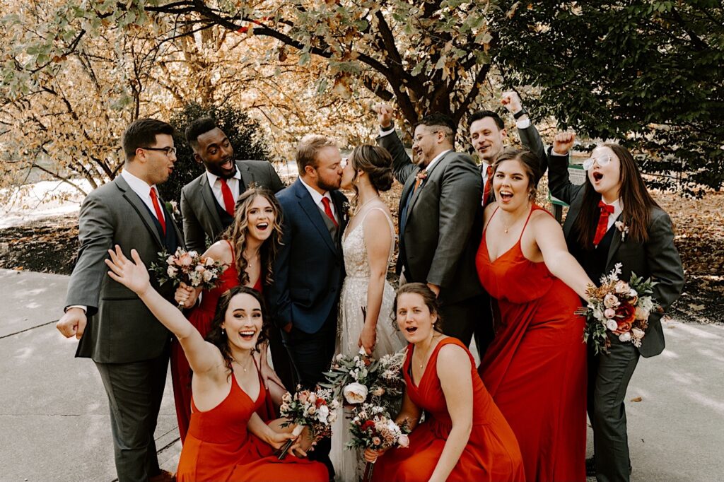 A bride and groom kiss as their wedding parties surround them and cheer during their fall wedding day, photographed by a Chicago wedding photographer