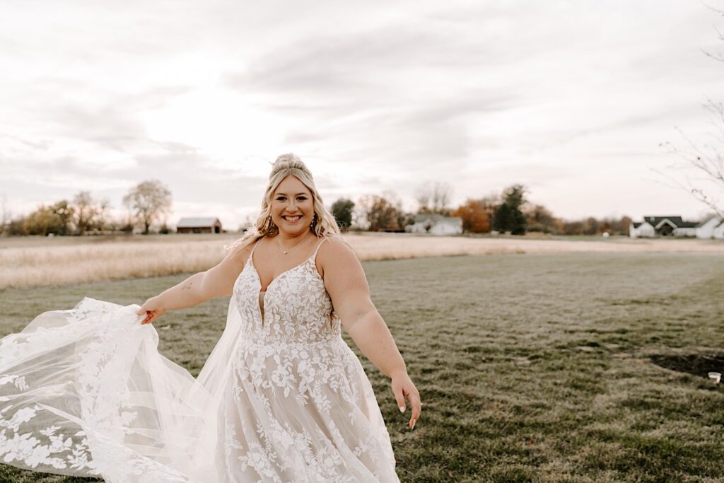 A bride in a field smiles at the camera as she spins and her dress flows in the wind, photographed by a Chicago wedding photographer