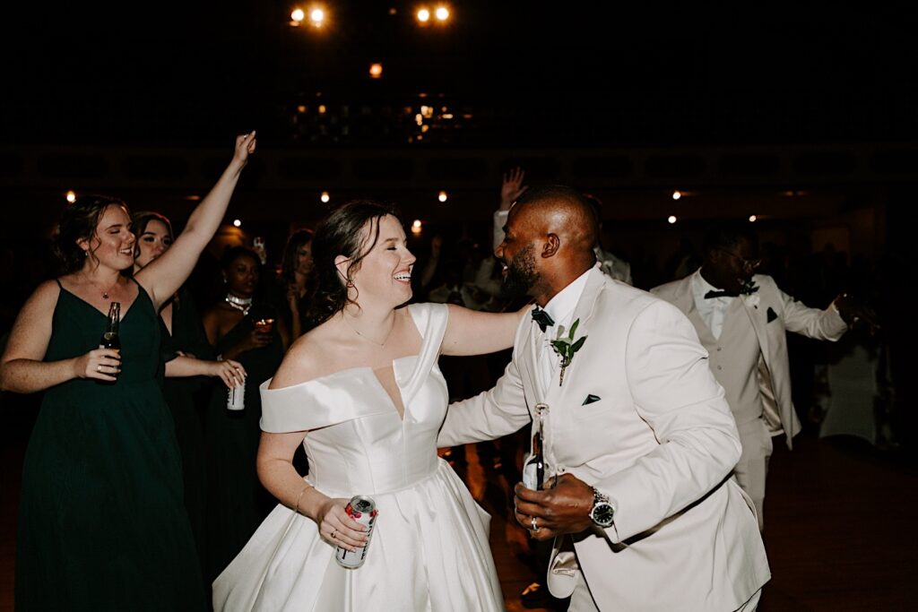 A bride and groom smile at one another as they dance with their wedding guests during their indoor wedding reception, photographed by a Chicago wedding photographer