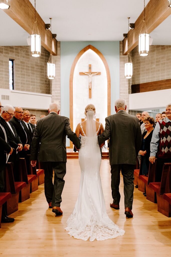 A bride is escorted down the aisle of a church on her wedding day by  her grandfathers on either side of her