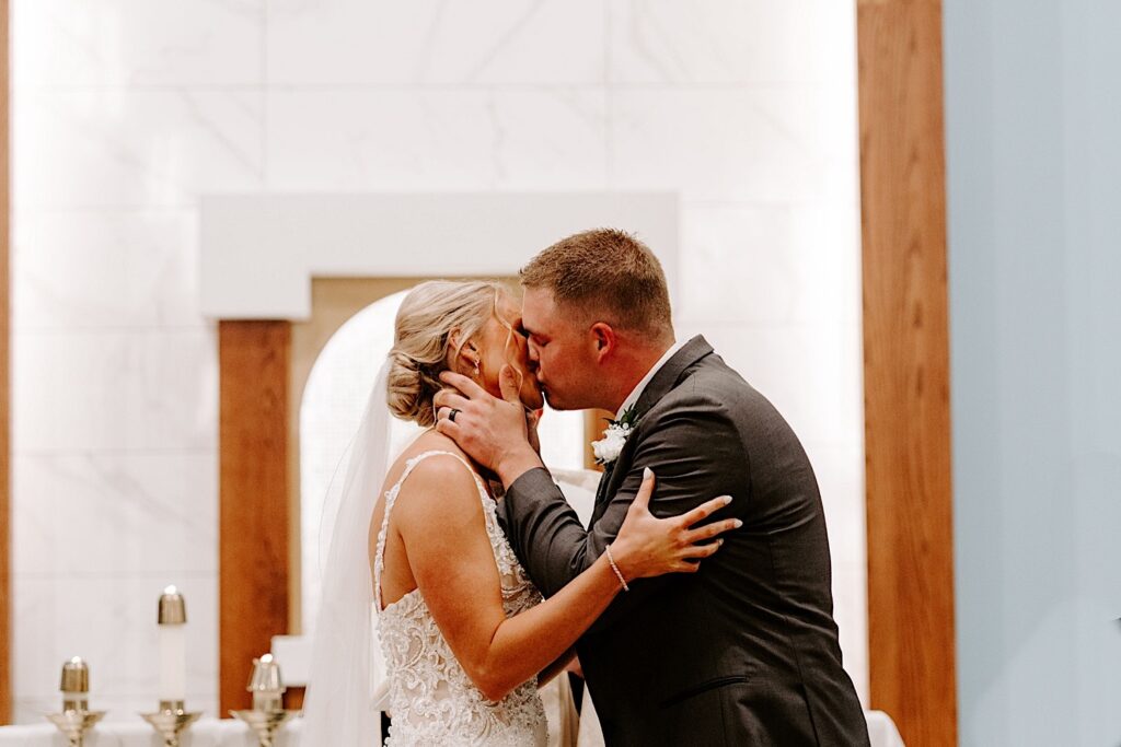 A bride and groom kiss one another in a church during their wedding ceremony