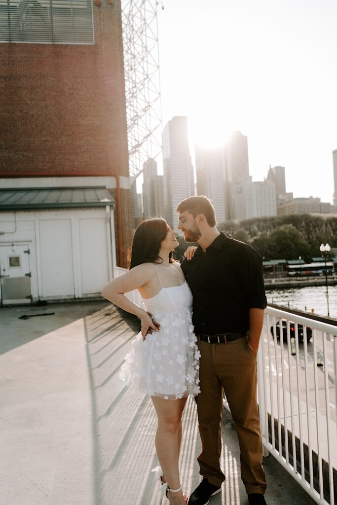 A couple stand next to one another and smile at each other with the Chicago skyline behind them