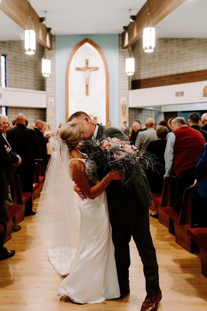 A bride and groom kiss one another while walking down the aisle of a church after their wedding ceremony