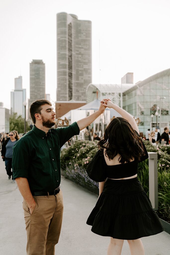 A man dances with his fiancée at Navy Pier in Chicago with the skyline of the city behind them