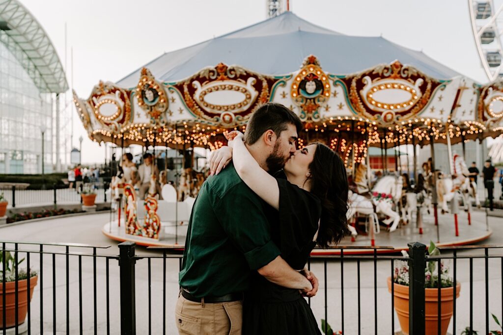 A couple kiss and embrace in front of the carousel at Navy Pier in Chicago during their engagement session