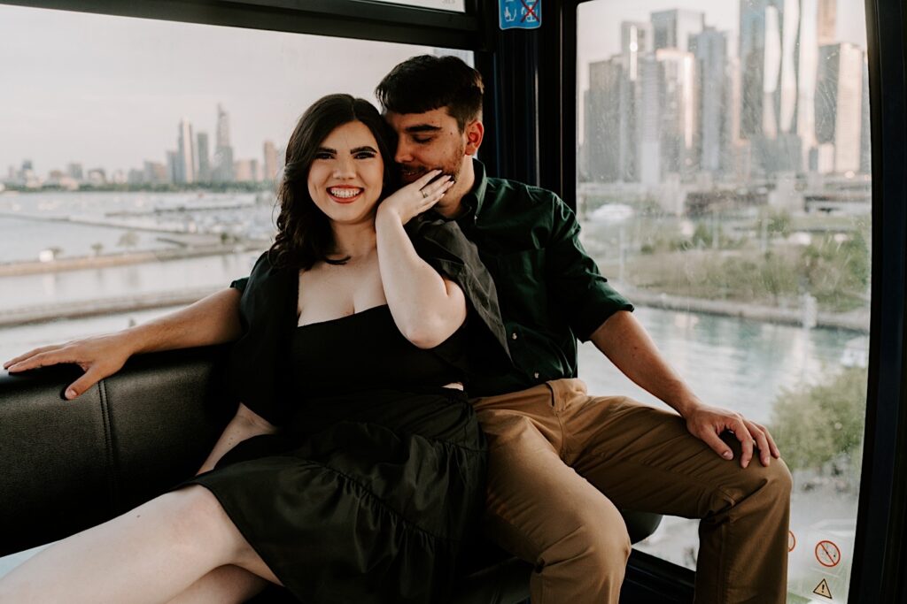 A couple snuggle next to one another and smile at the camera as they ride the Ferris Wheel at Navy Pier in Chicago during their engagement session
