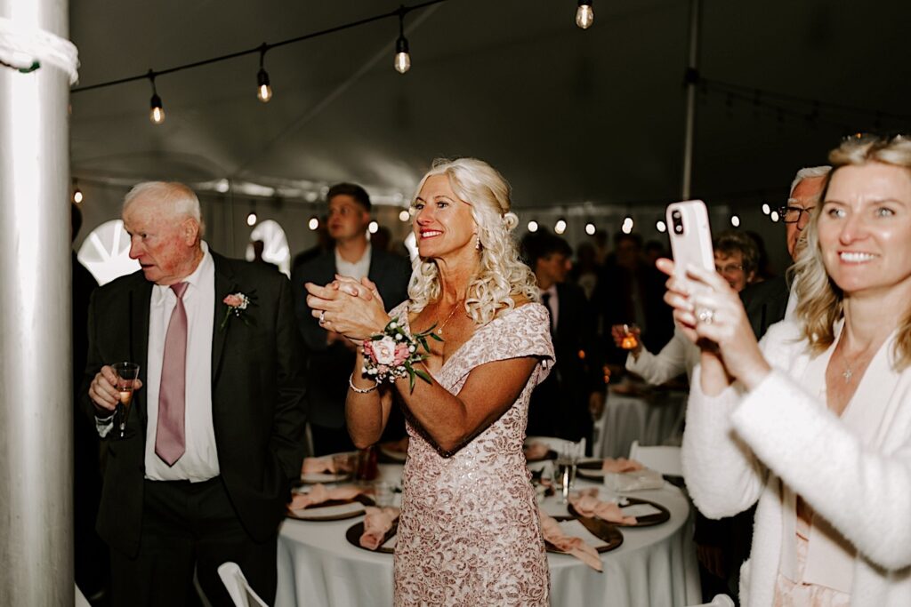 The mother of the bride stands and claps during a backyard tent wedding reception