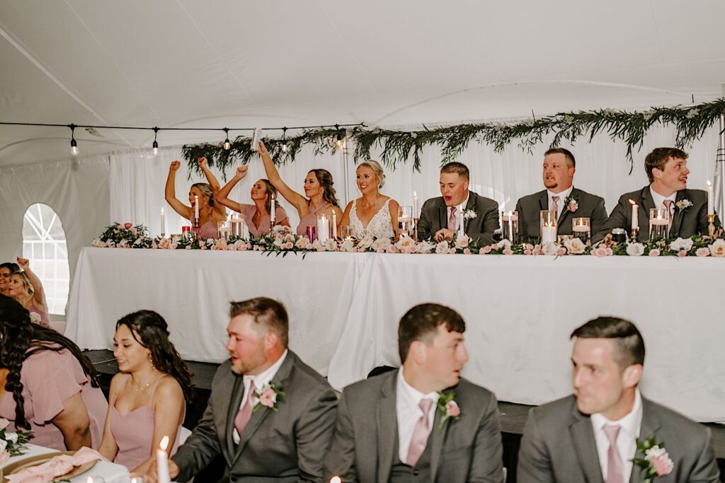 A bride and groom are seated at the head table with bridesmaids and groomsmen on either side of them 