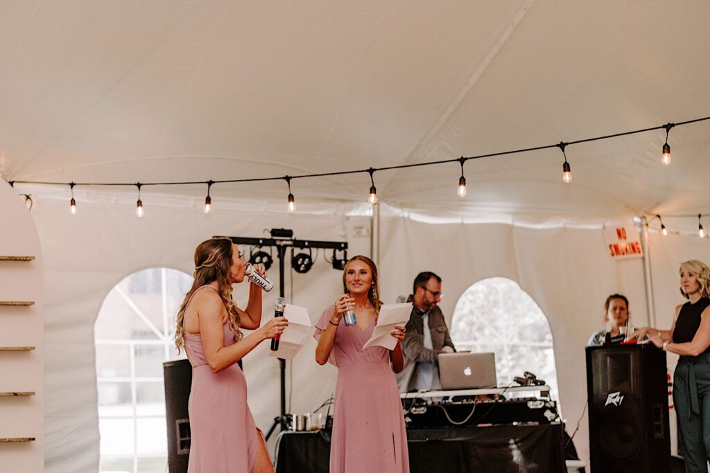 Two bridesmaids drink while holding their speech papers during a wedding reception 
