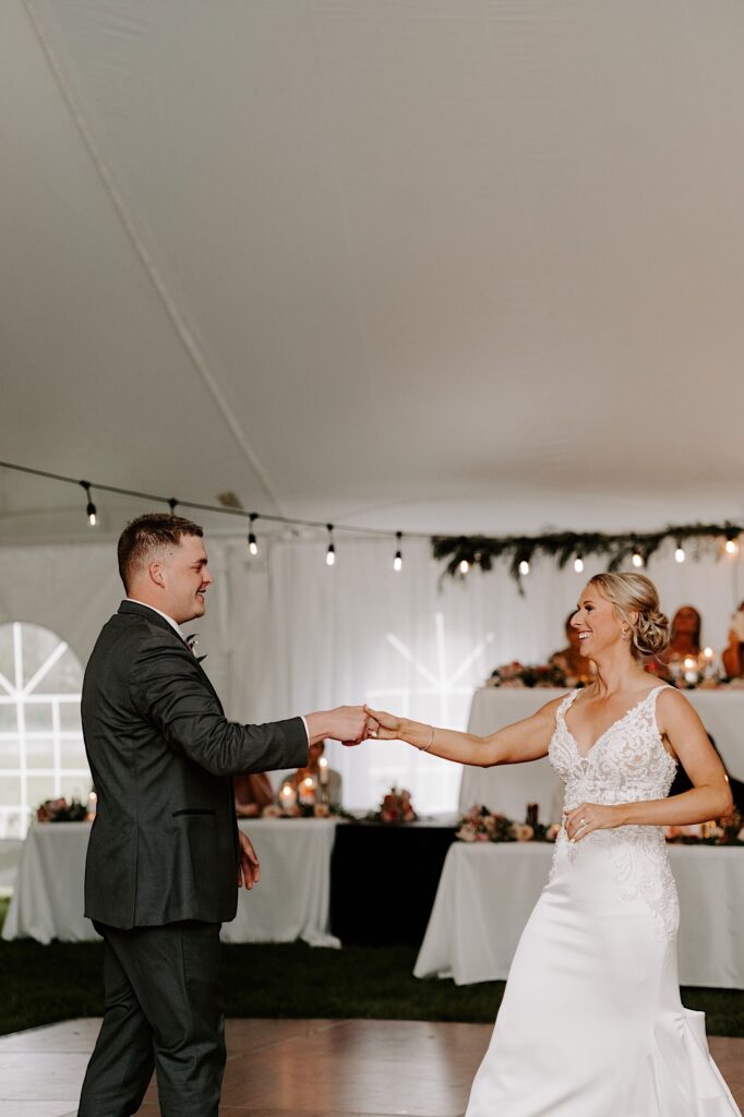A bride and groom smile as they share their first dance together while underneath their wedding tent