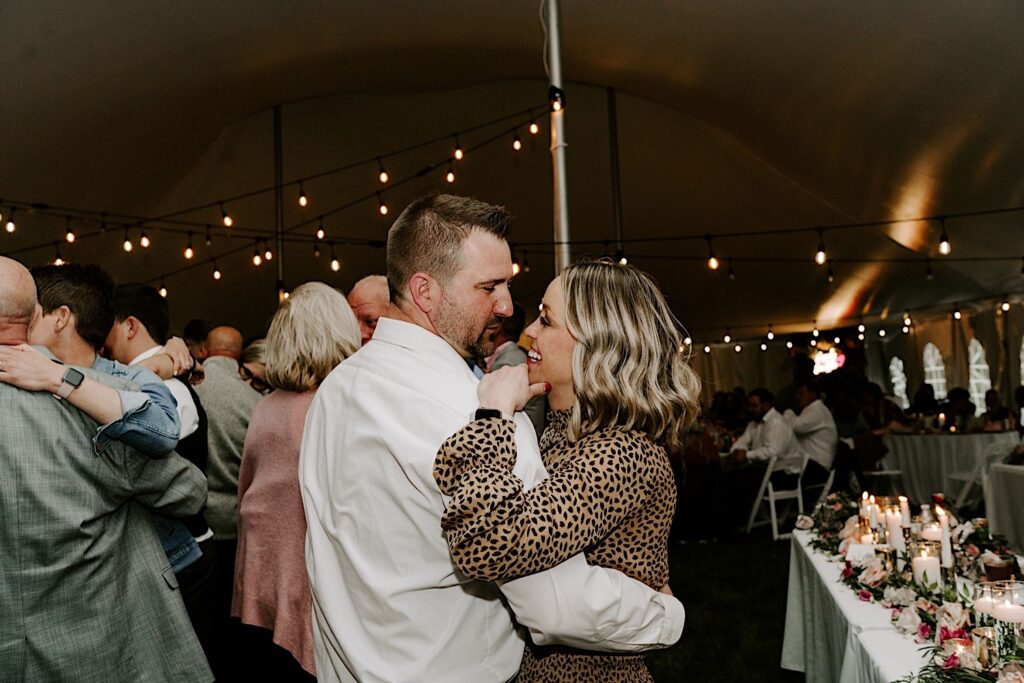 A couple smile at one another while dancing during a backyard tent wedding reception