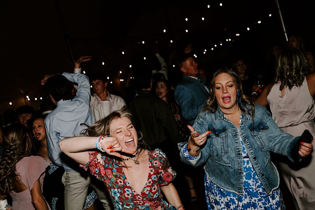 Guests of a backyard tent wedding dance and yell together underneath string lights