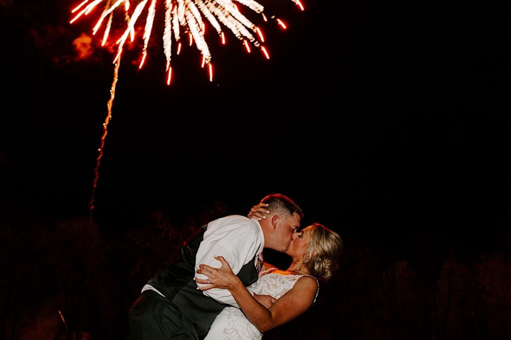 A bride and groom kiss and dip as a firework explodes overhead