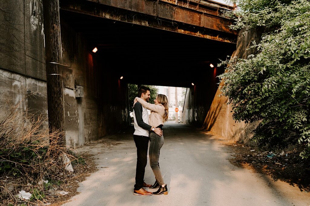 A couple embrace and smile at one another while under an old metal bridge in Chicago