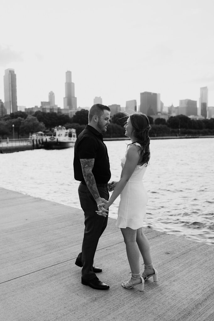 Black and white photo of a couple standing together and holding hands in front of Lake Michigan and the Chicago skyline