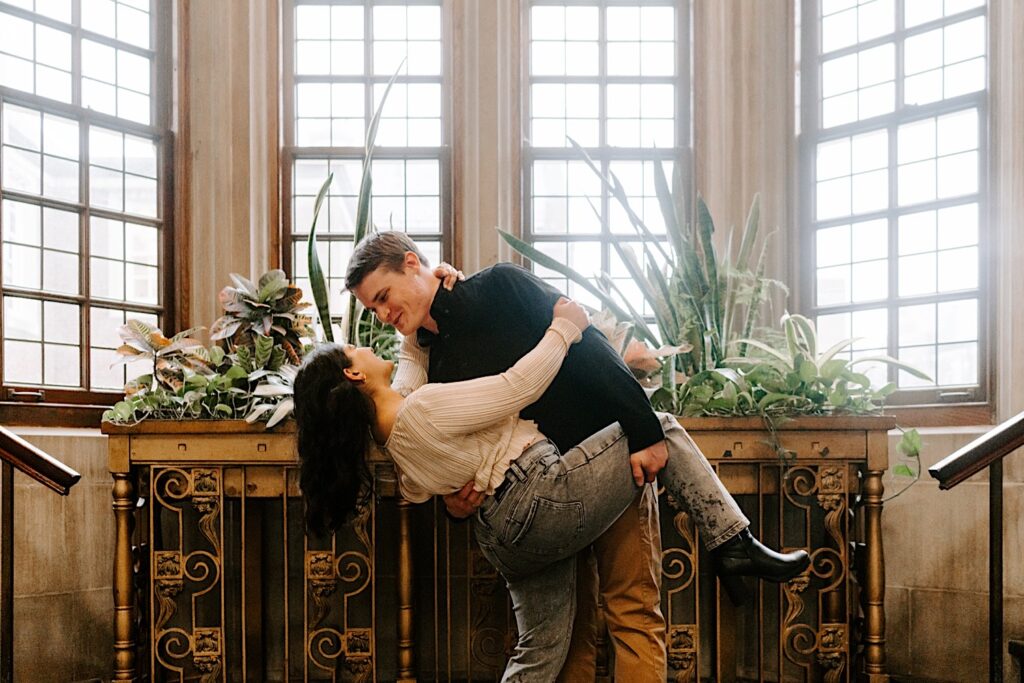 Next to an indoor planter a man dips a woman as they smile at one another inside a building in Chicago while taking their engagement photos