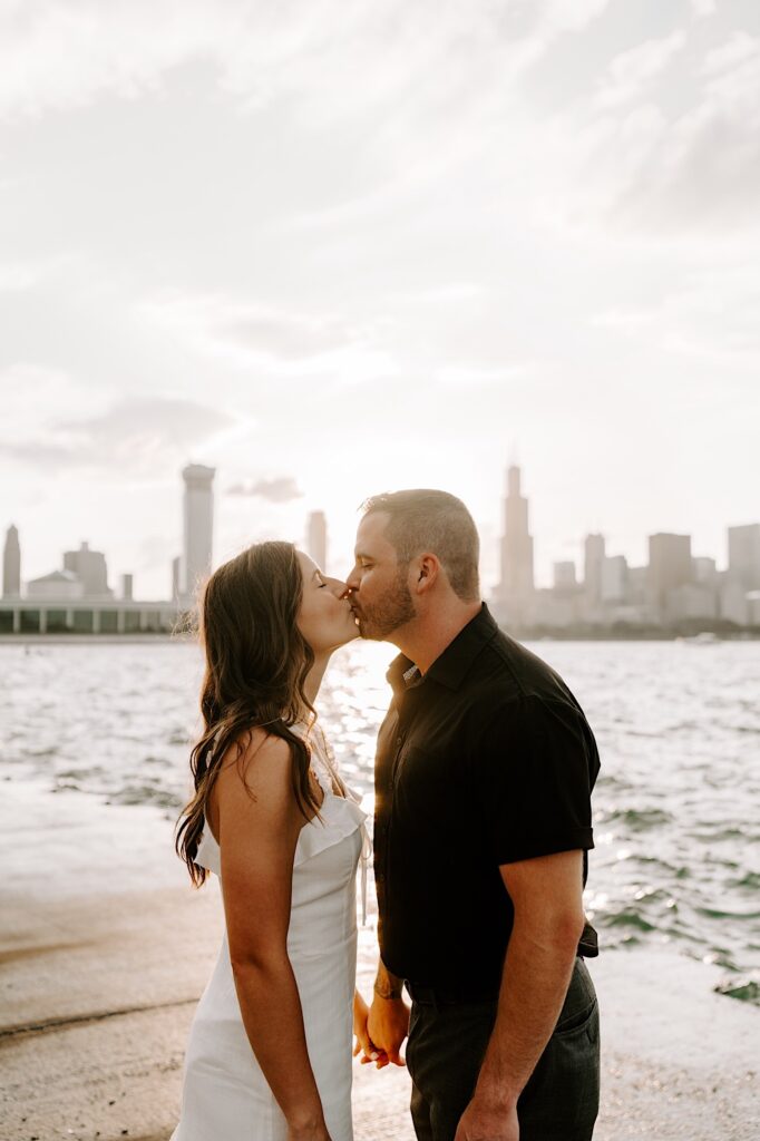 A man and woman kiss as the sun sets behind them over the Chicago skyline and Lake Michigan