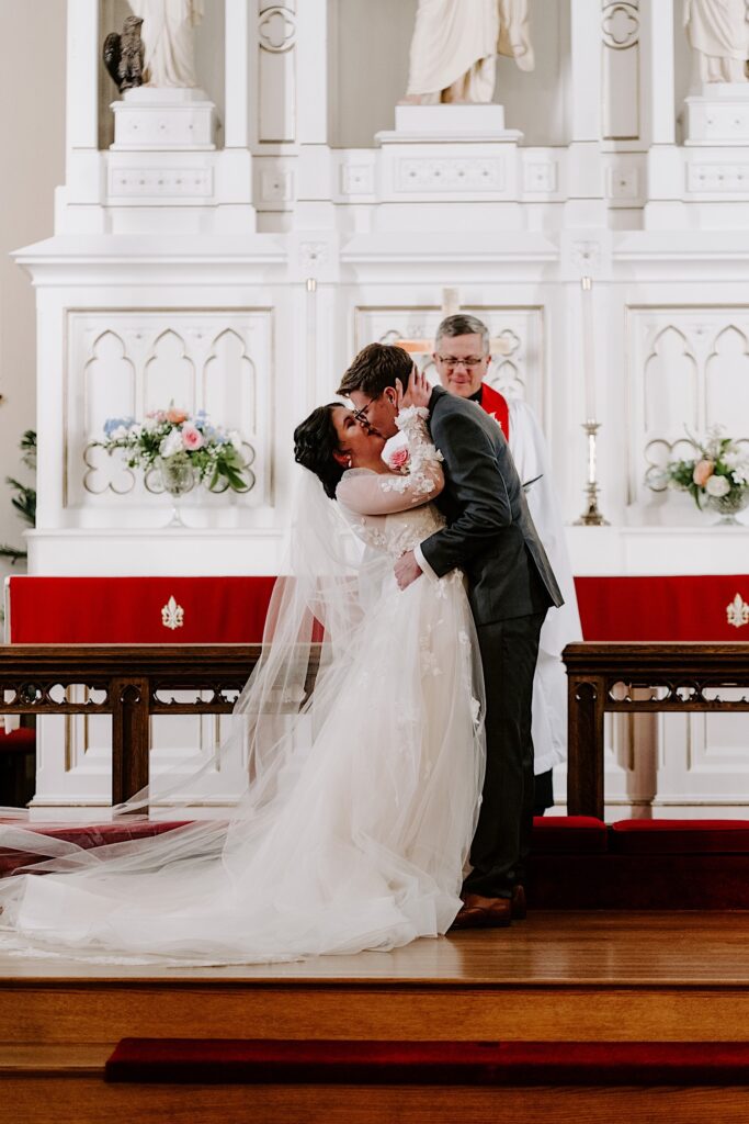 A bride and groom kiss one another during their wedding ceremony in a church