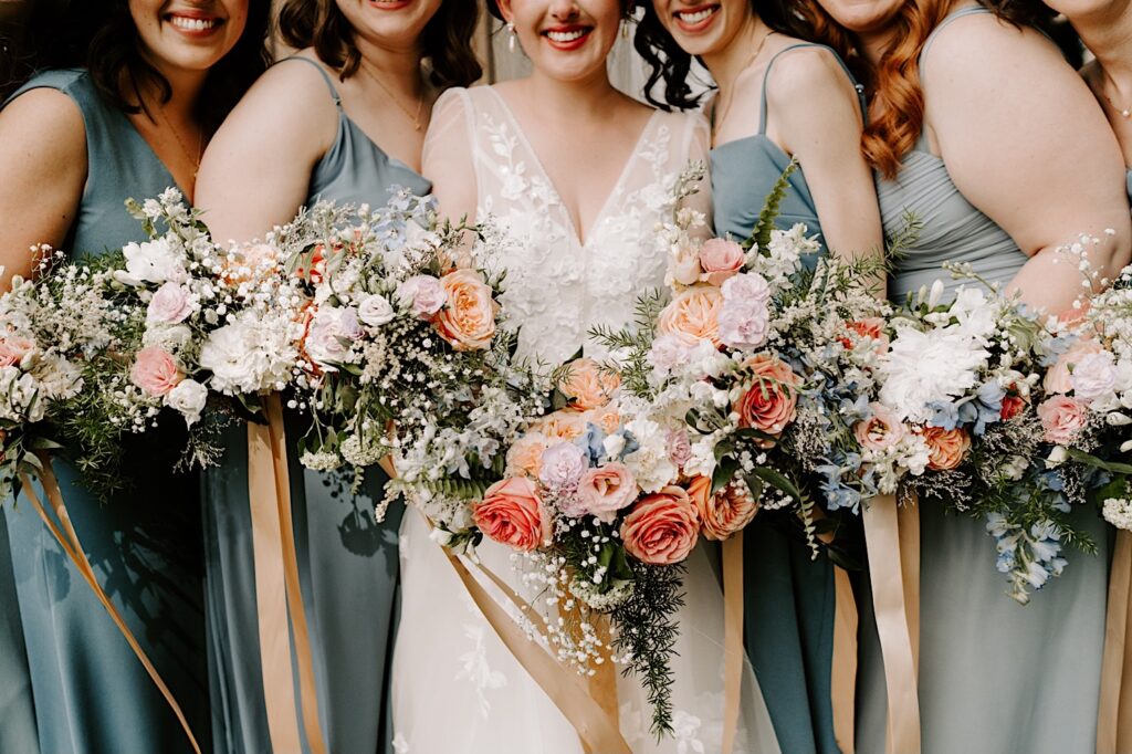 Close up photo of a bride and her bridesmaids smiling at the camera while holding their bouquets towards the camera
