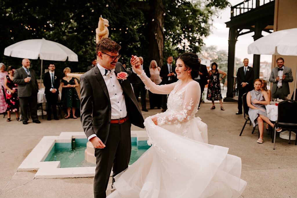 During their outdoor wedding reception at the Fowler House Mansion, a bride and groom smile while dancing surrounded by the guests of their wedding