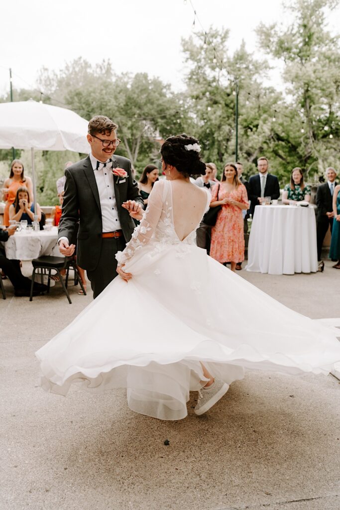 During their outdoor wedding reception a bride and groom dance and the bride spins her dress while the groom smiles at her